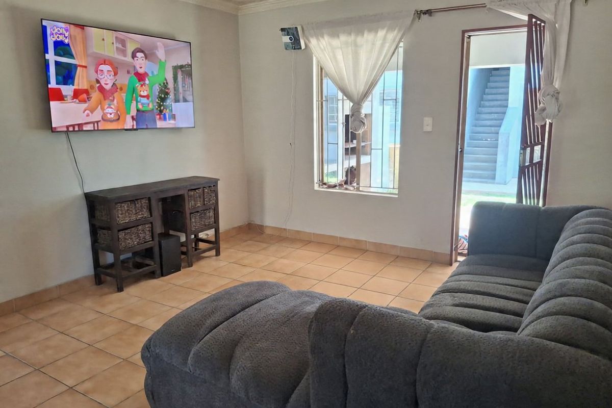 A living room featuring ceramic floor tiles, security bars on the window, and a security gate leading to an exterior walkway.