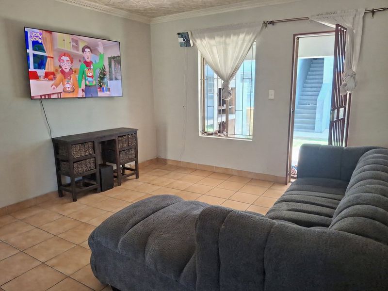 A living room featuring ceramic floor tiles, security bars on the window, and a security gate leading to an exterior walkway.