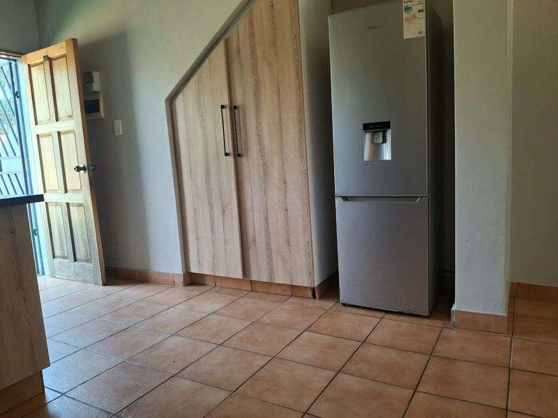 A kitchen area featuring light wood-finish built-in cabinetry, tiled flooring, and a wooden door leading to the exterior.