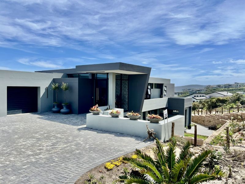 A modern, architecturally designed home featuring a paved driveway, integrated garage, and a striking contemporary facade with clean lines and a landscaped entrance.