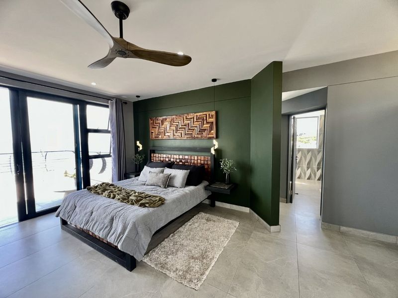 Modern bedroom featuring large sliding glass doors, tiled flooring, a ceiling fan, and an en-suite bathroom entrance with a bold green accent wall.