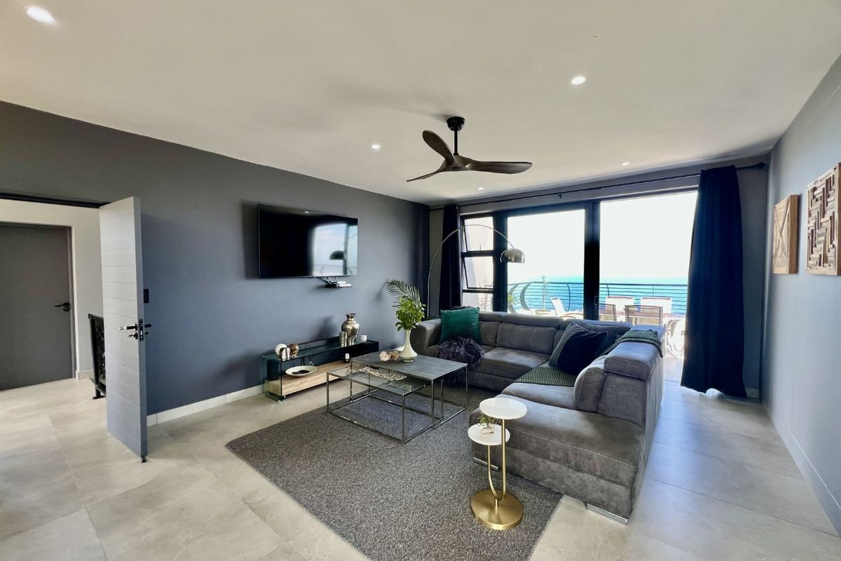 Modern living room featuring large sliding glass doors with ocean views, recessed lighting, a ceiling fan, and neutral tiled flooring.
