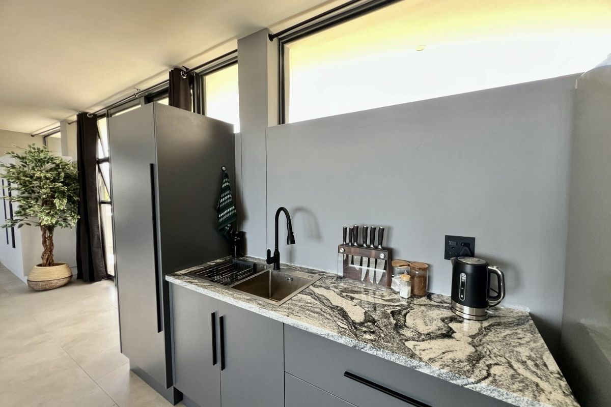 Modern kitchen area featuring sleek grey cabinetry, a striking granite countertop, undermount sink with gooseneck faucet, and high-level clerestory windows.