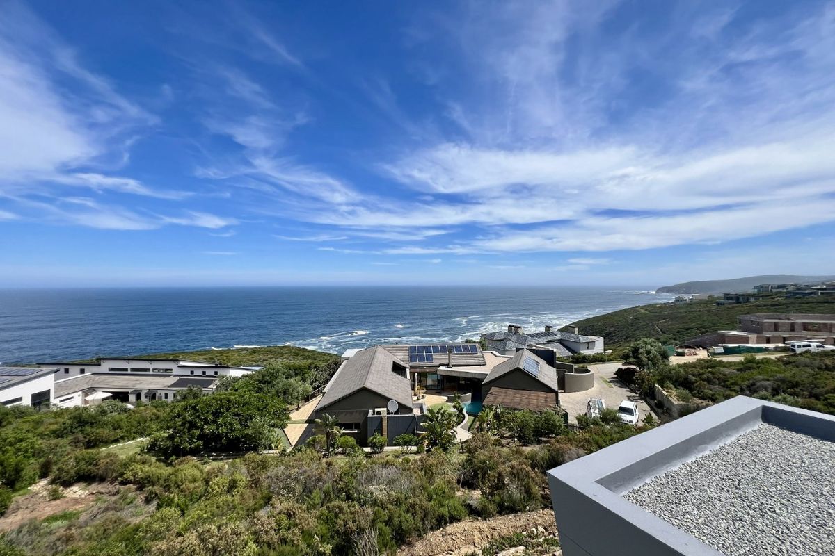 Aerial view of a coastal property featuring a tiled roof with solar panels, a swimming pool, and expansive ocean views.