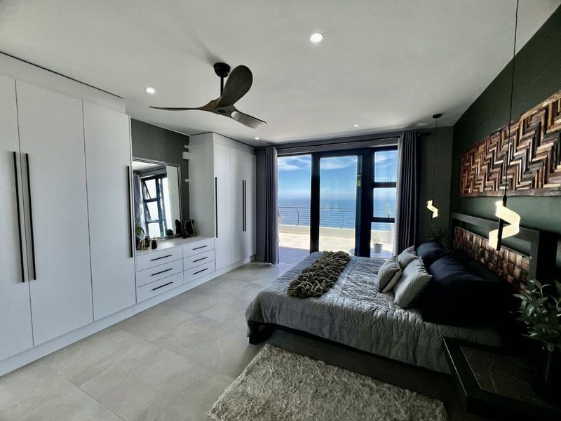 Modern bedroom featuring built-in cupboards, tiled flooring, and large sliding glass doors opening onto a balcony with scenic ocean views.