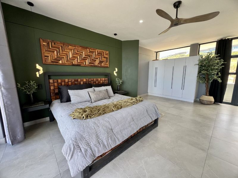 Spacious modern bedroom featuring large format floor tiles, built-in cabinetry, a ceiling fan, and a striking green accent wall with integrated lighting.