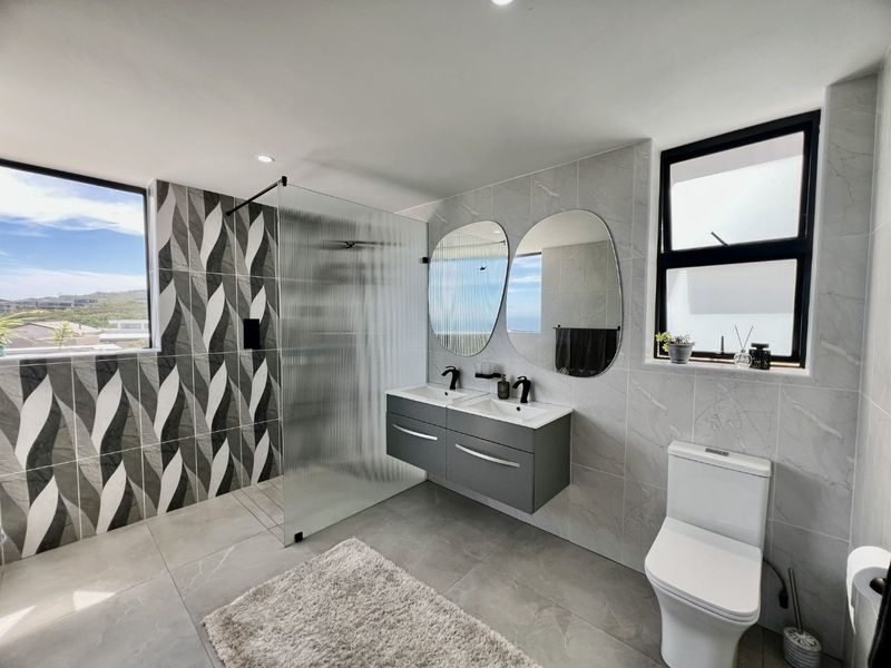 Modern bathroom featuring a double vanity with black tapware, a spacious walk-in shower with fluted glass screen, and contemporary grey tiling.