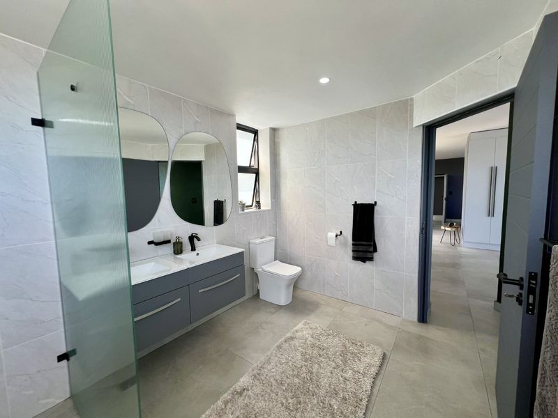 Modern bathroom featuring a double vanity with wall-mounted cabinetry, a glass shower screen, and contemporary tiled finishes throughout.