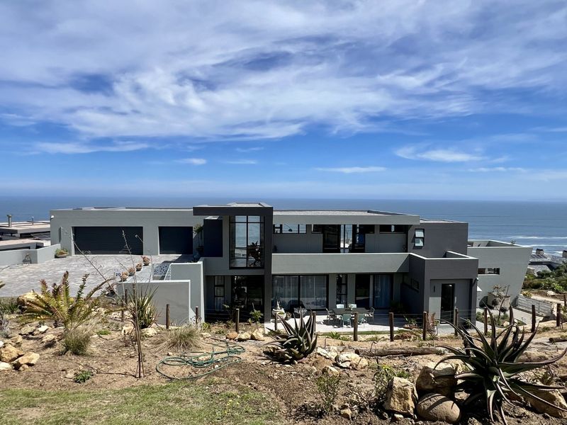 Modern multi-level coastal residence featuring a flat roof, expansive glass windows, double garage, and a rear patio overlooking the ocean.