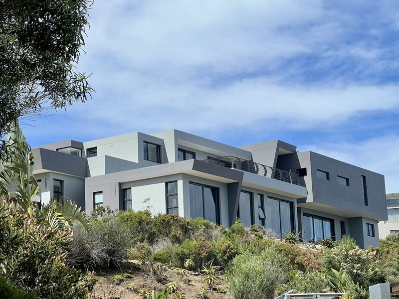 A modern multi-level residential property featuring contemporary architectural design, large glass sliding doors, and an elevated balcony overlooking a landscaped garden.