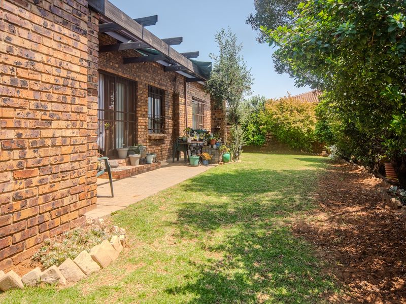 A private rear garden featuring a paved patio area, timber pergola, and established lawn, enclosed by a brick boundary wall.