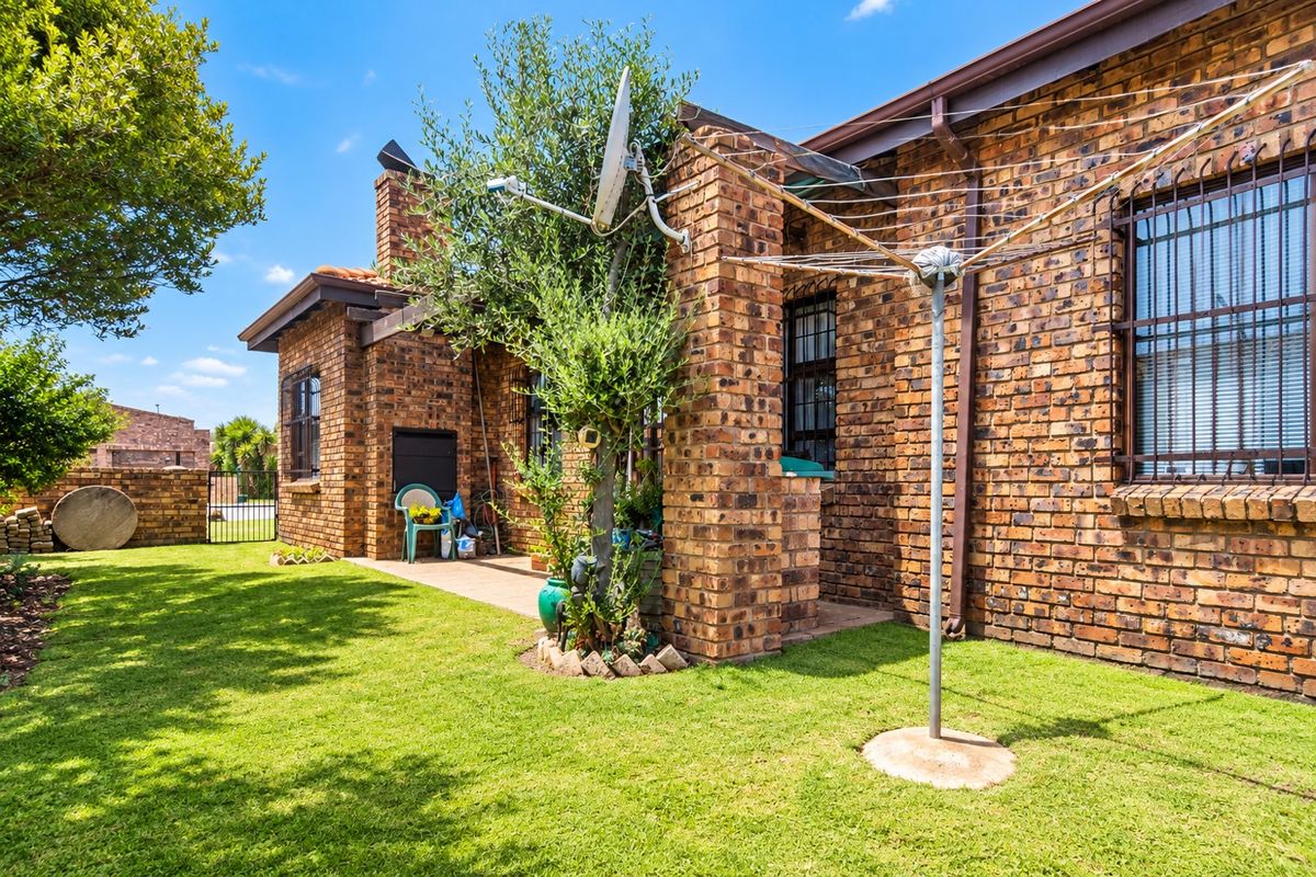 A well-maintained rear exterior featuring a face brick facade, a paved patio area with a built-in braai, and a neat garden.