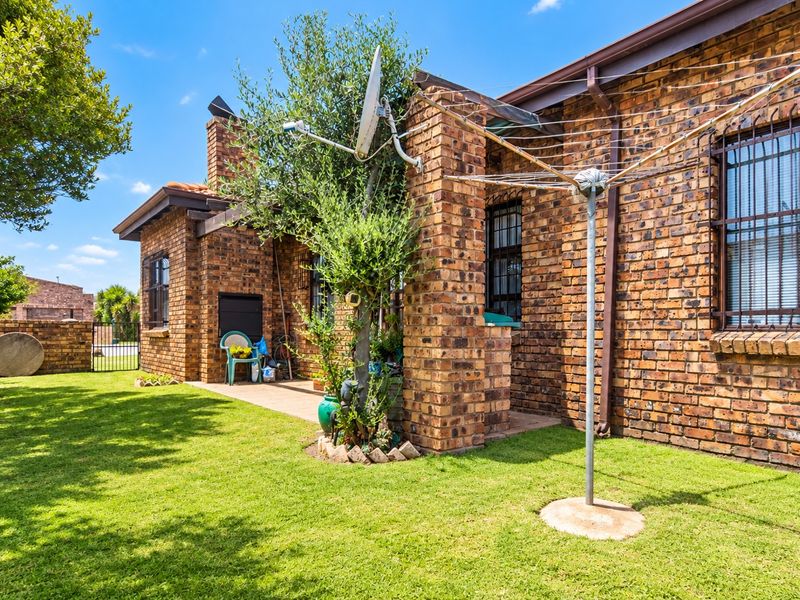 A well-maintained rear exterior featuring a face brick facade, a paved patio area with a built-in braai, and a neat garden.
