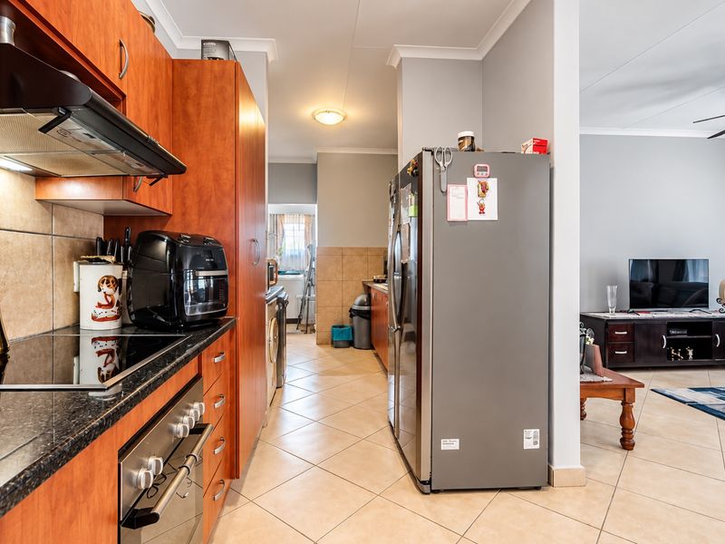 A functional kitchen featuring wood-finish cabinetry, granite countertops, and integrated appliances, flowing into an adjacent living area with tiled flooring throughout.
