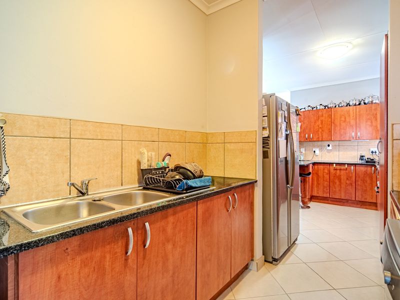 A functional scullery area featuring double stainless steel sinks, granite countertops, and ample wooden cabinetry, providing additional prep and storage space adjacent to the kitchen.