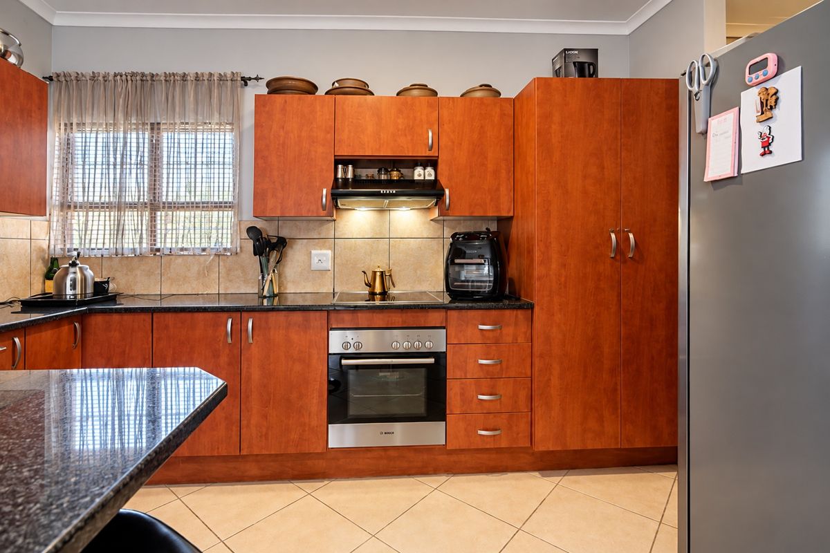 A functional kitchen featuring warm-toned wooden cabinetry, granite countertops, a built-in oven with hob, and tiled flooring, offering a practical and well-maintained workspace.