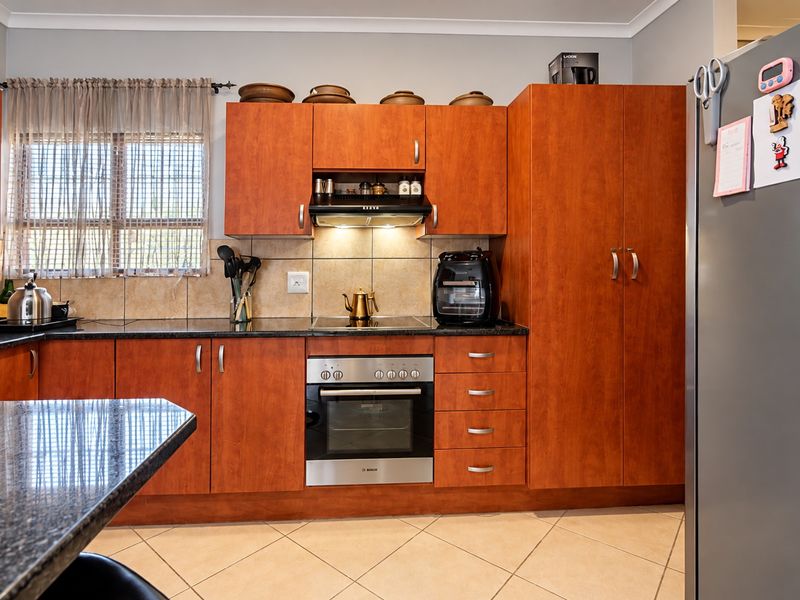 A functional kitchen featuring warm-toned wooden cabinetry, granite countertops, a built-in oven with hob, and tiled flooring, offering a practical and well-maintained workspace.