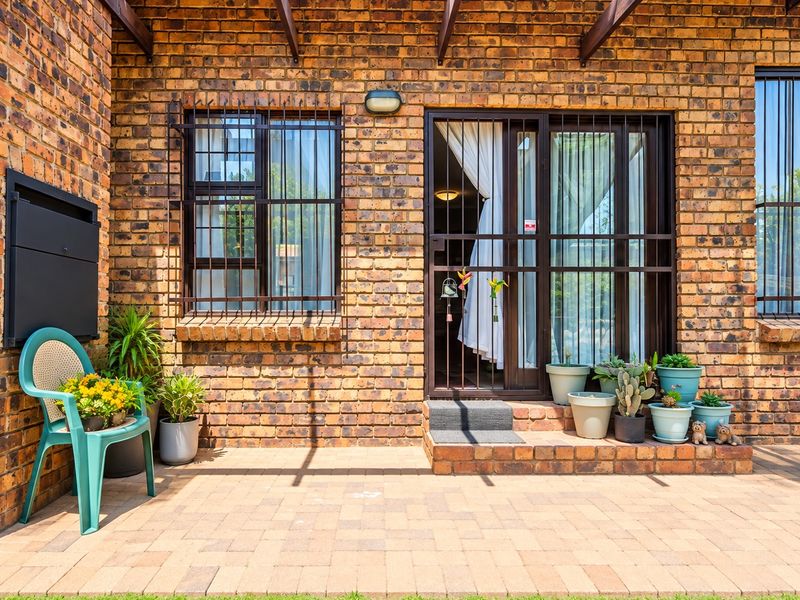 A well-maintained face brick patio area featuring a timber pergola, secure window and door bars, and paved flooring.