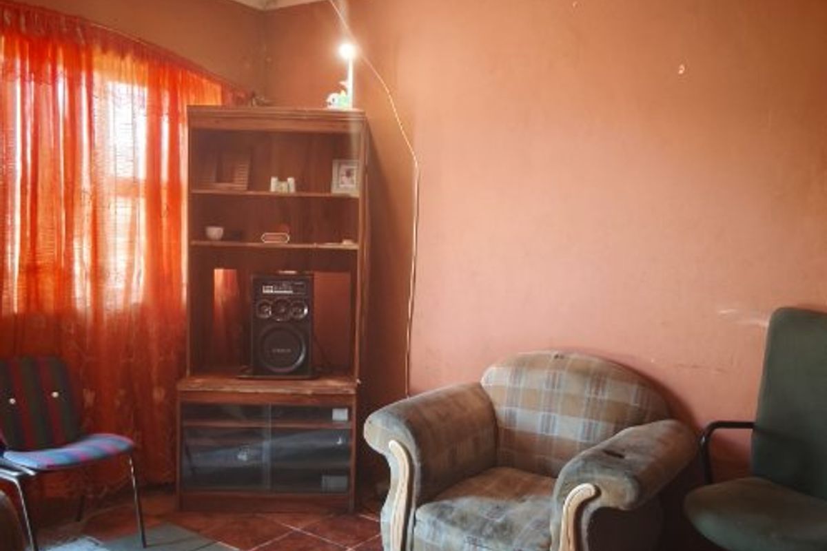 A living room space featuring tiled flooring and a ceiling rose, currently requiring significant cosmetic updates and repairs to the walls and ceiling.
