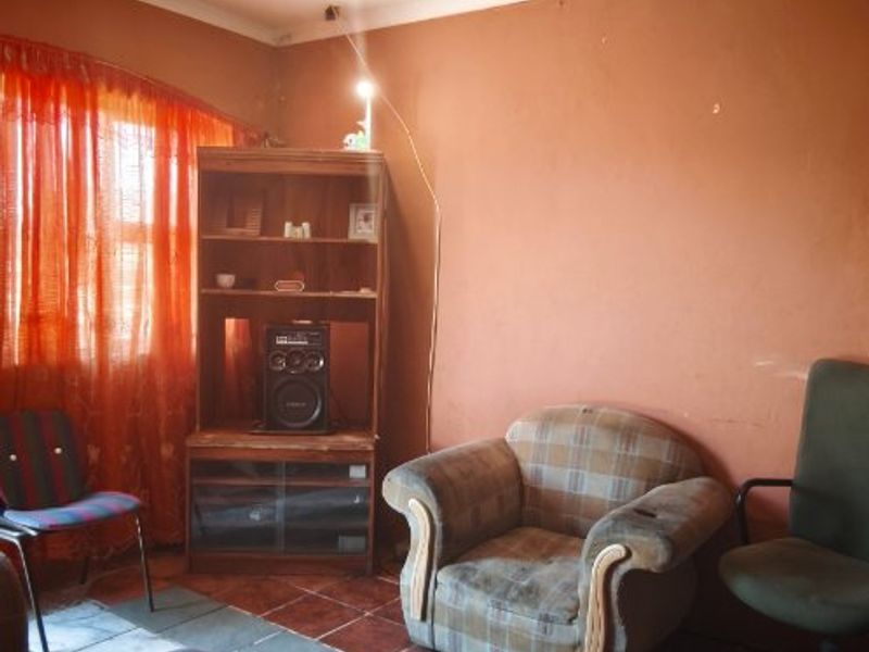 A living room space featuring tiled flooring and a ceiling rose, currently requiring significant cosmetic updates and repairs to the walls and ceiling.