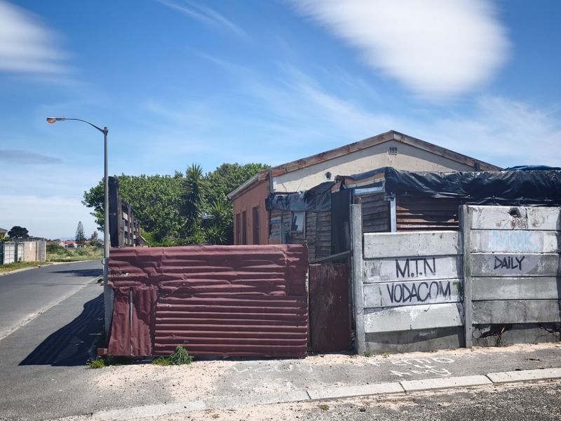 Street view of a residential property featuring a precast concrete boundary wall with graffiti and corrugated metal fencing.
