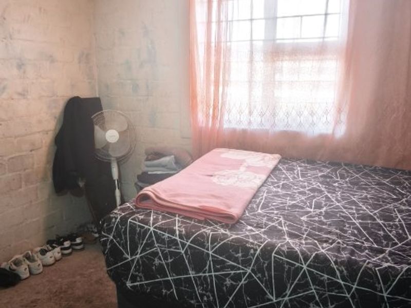 A bedroom featuring a window with security bars and coving, currently requiring significant cosmetic updates to the walls and flooring.