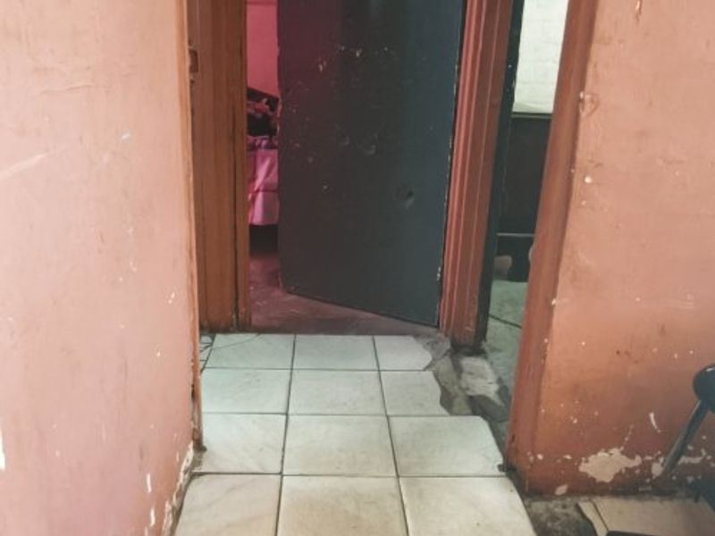 A narrow hallway featuring ceramic floor tiles and walls showing significant signs of wear, including peeling paint and damaged plaster.