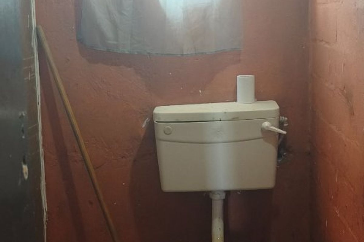 A small, basic bathroom featuring a ceramic toilet and tiled flooring, requiring significant renovation and cosmetic updates to improve functionality and appearance.