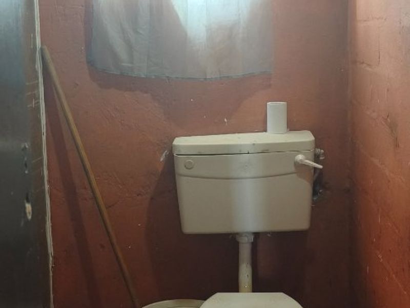 A small, basic bathroom featuring a ceramic toilet and tiled flooring, requiring significant renovation and cosmetic updates to improve functionality and appearance.