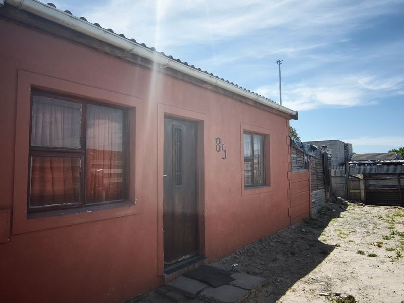 Front elevation of a single-story residential property featuring plastered walls, a corrugated metal roof, and aluminium window frames.