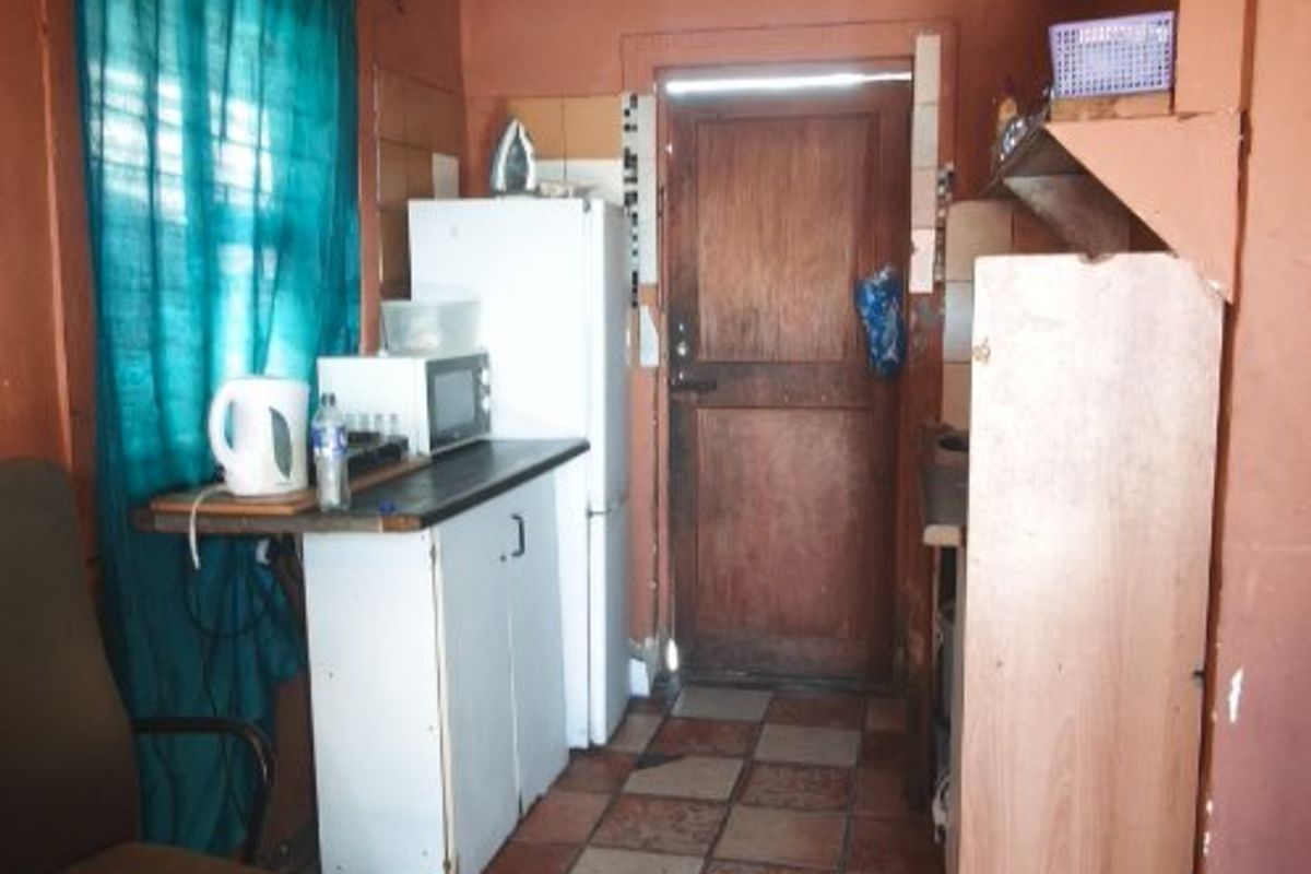 A compact kitchen area featuring tiled flooring, built-in cabinetry, and a wooden exterior door, currently requiring maintenance and cosmetic updates.