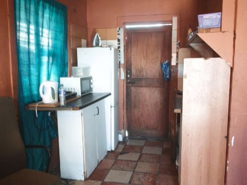 A compact kitchen area featuring tiled flooring, built-in cabinetry, and a wooden exterior door, currently requiring maintenance and cosmetic updates.