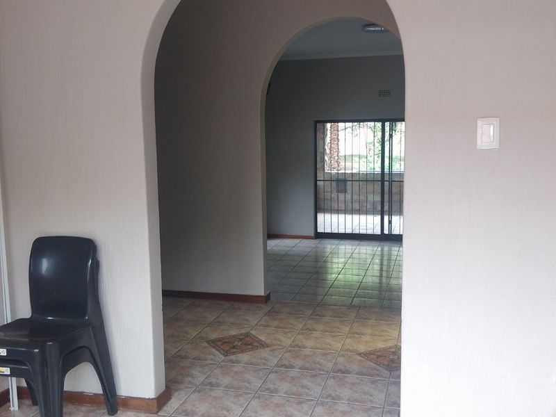 A neutral-toned hallway featuring an arched transition between spaces, ceramic tiled flooring, and a secure rear exit point.