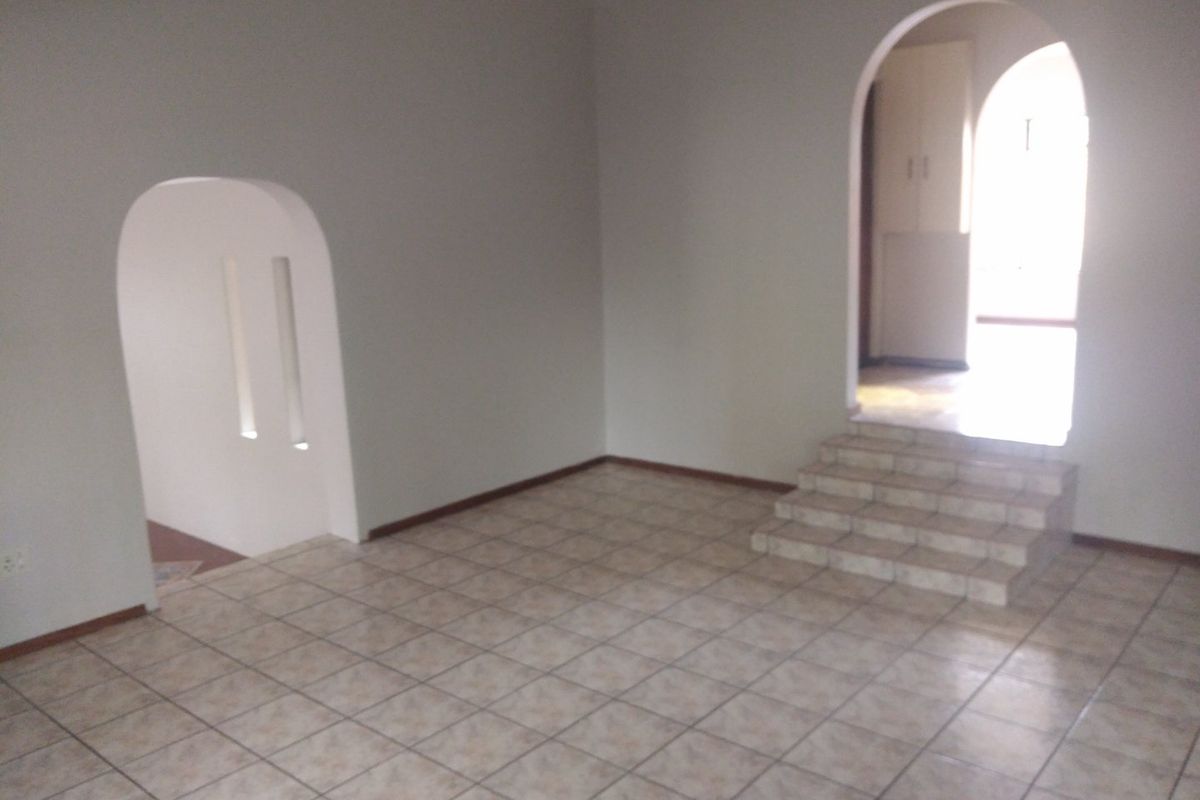 An empty living area featuring tiled flooring, arched architectural doorways, and a small set of tiled steps leading to an adjacent space.