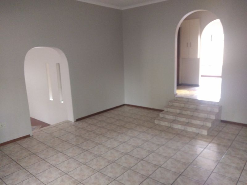 An empty living area featuring tiled flooring, arched architectural doorways, and a small set of tiled steps leading to an adjacent space.
