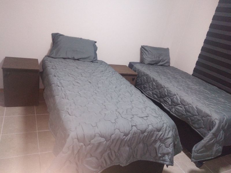 A bedroom featuring tiled flooring and modern roller blinds, currently furnished with two single beds.