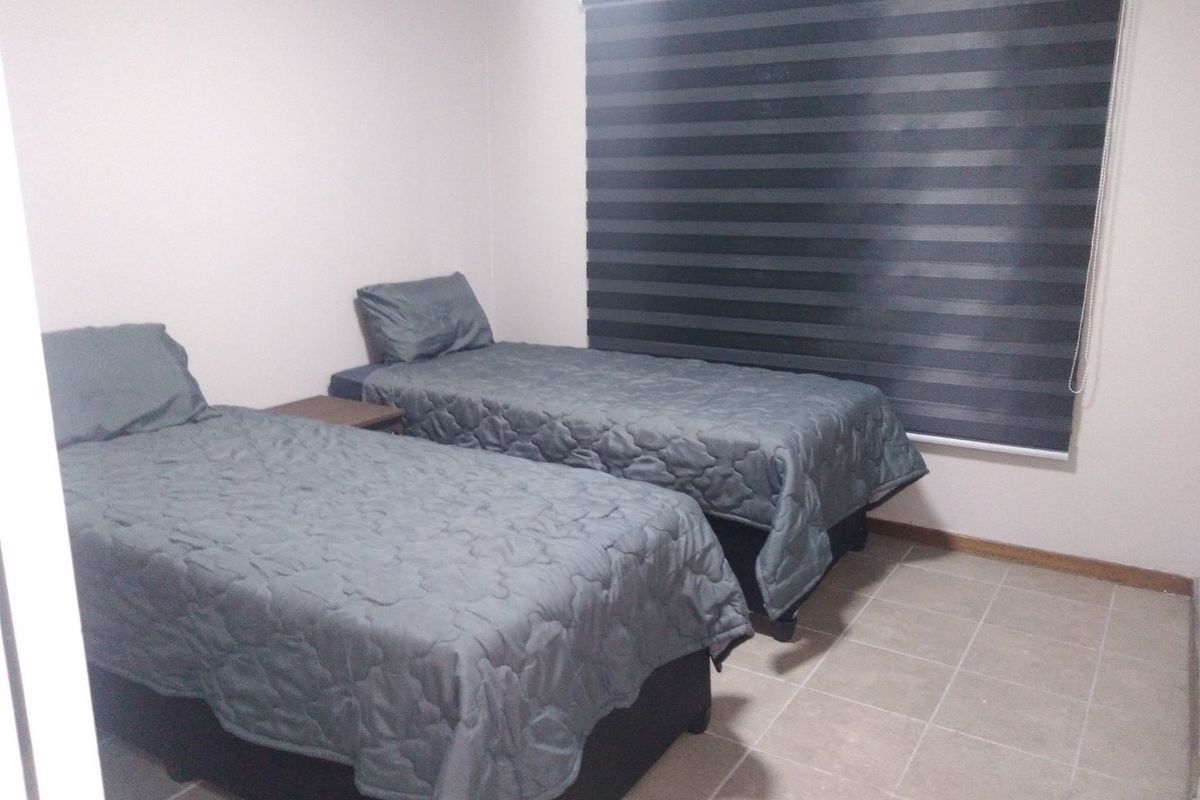 A functional bedroom featuring tiled flooring and modern zebra blinds, providing a neutral space ready for personalization.