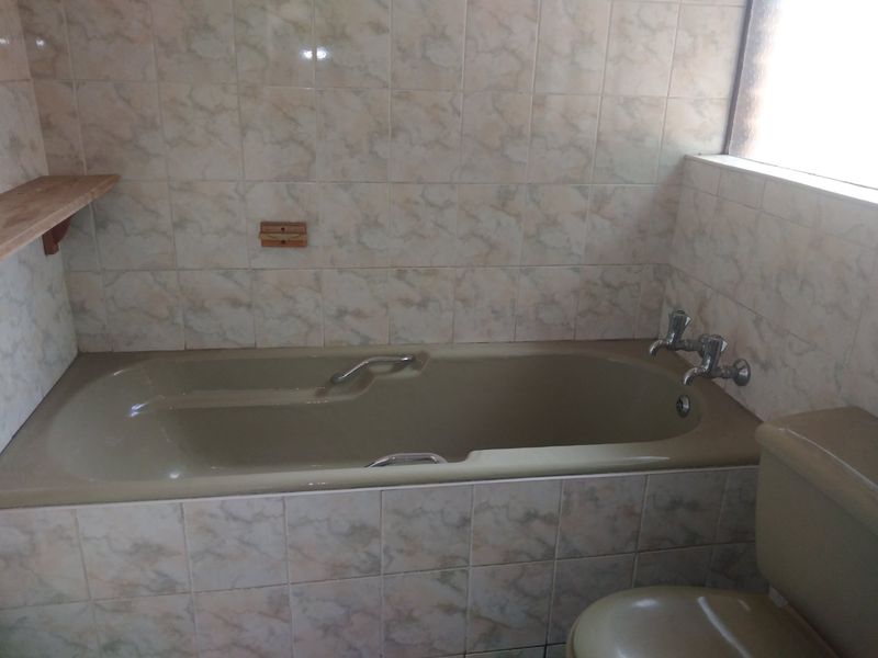 A dated bathroom featuring a built-in bathtub with wall-mounted taps and full-height ceramic wall tiling.