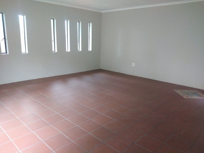 A spacious, empty living area featuring neutral walls, tiled flooring, and multiple vertical windows providing natural light.