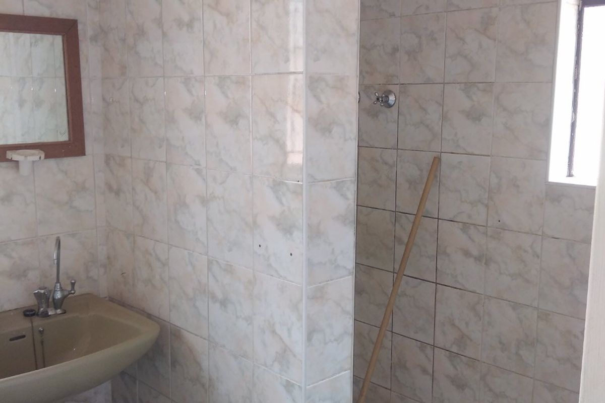 A functional bathroom featuring a pedestal basin and a tiled shower enclosure with dated finishes, offering potential for a modern renovation.