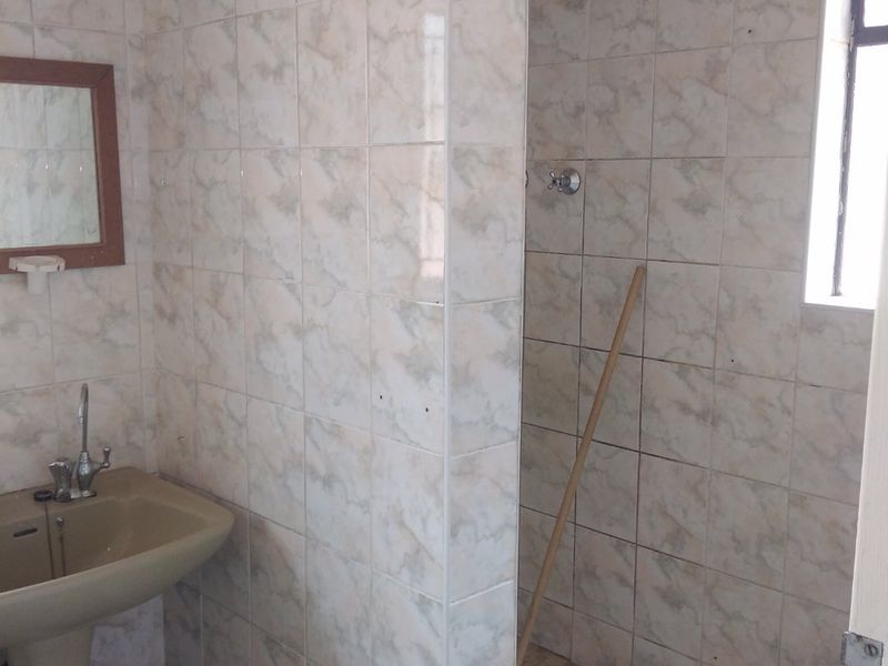 A functional bathroom featuring a pedestal basin and a tiled shower enclosure with dated finishes, offering potential for a modern renovation.