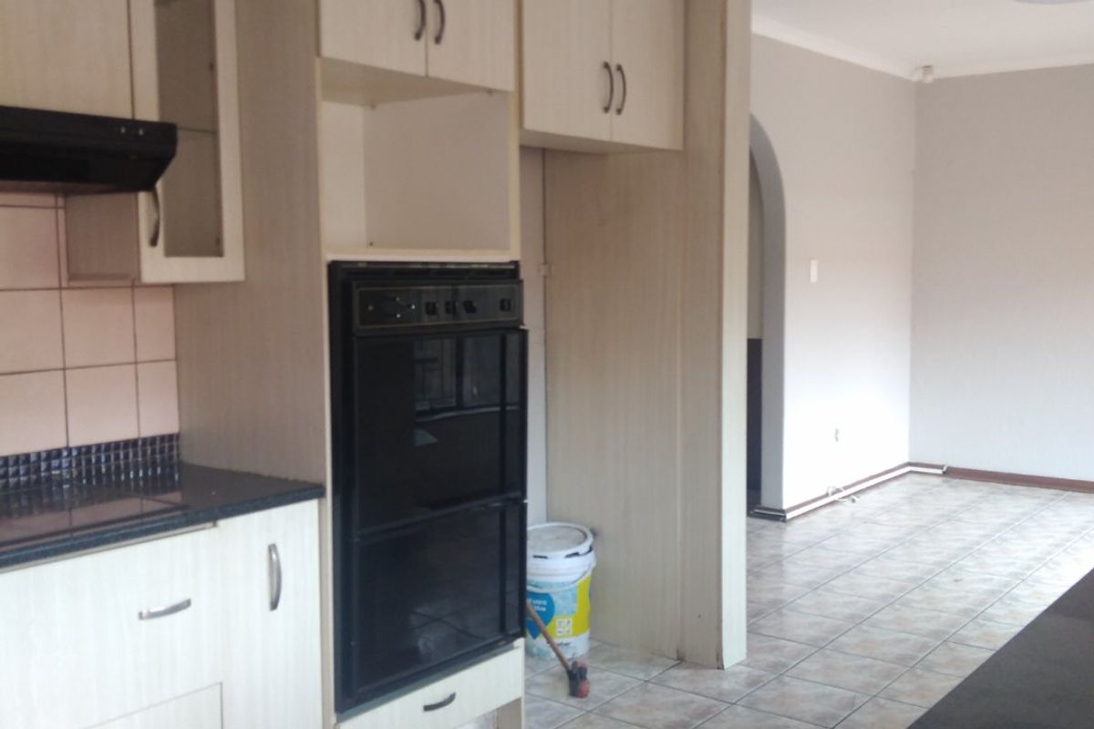 A functional kitchen featuring light wood-look cabinetry, built-in oven, extractor fan, and dark granite countertops, leading into an open-plan living area.