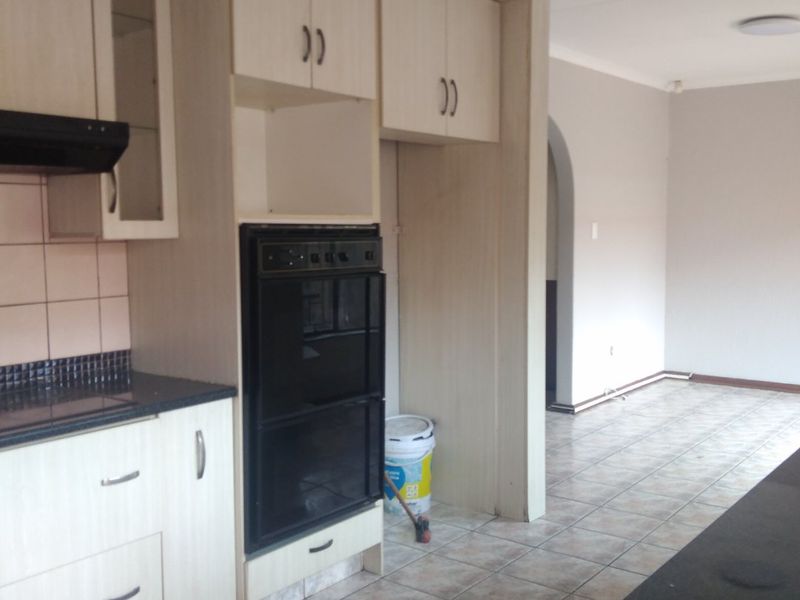 A functional kitchen featuring light wood-look cabinetry, built-in oven, extractor fan, and dark granite countertops, leading into an open-plan living area.