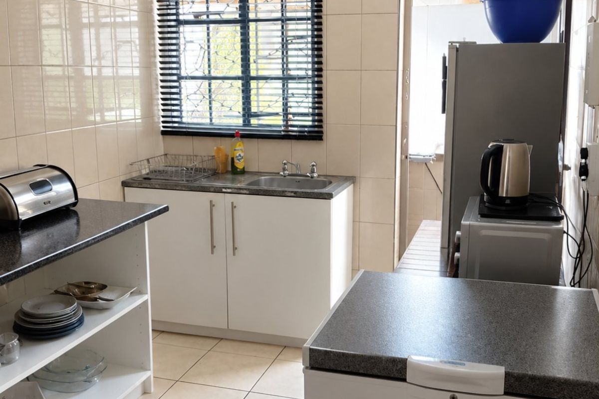 A functional kitchen featuring tiled walls and flooring, laminate countertops, and built-in cabinetry with a stainless steel sink.