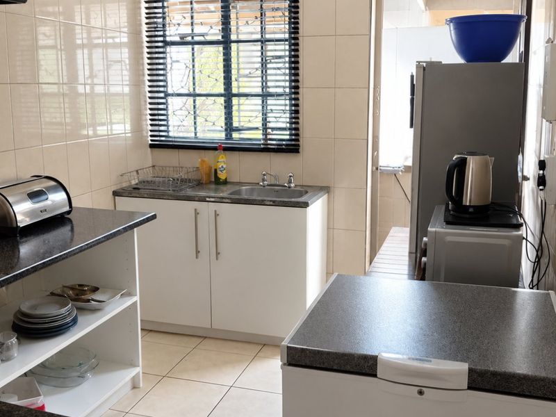 A functional kitchen featuring tiled walls and flooring, laminate countertops, and built-in cabinetry with a stainless steel sink.
