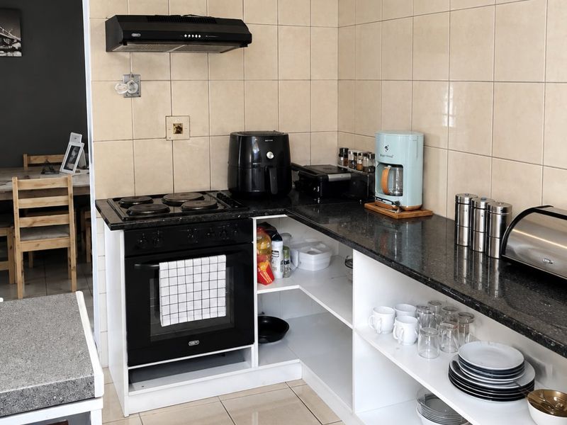 A functional kitchen featuring granite countertops, a built-in oven with hob, extractor fan, and open shelving, finished with tiled splashbacks and flooring.