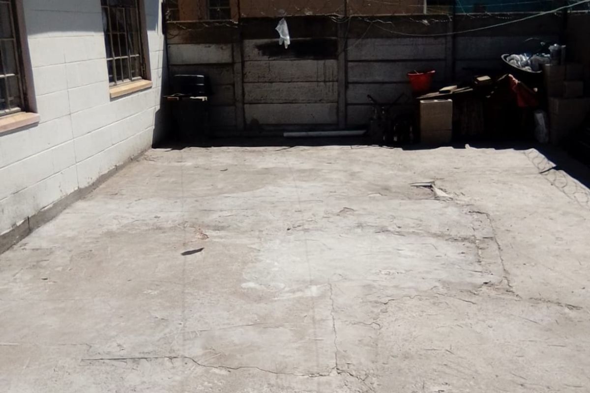 A rear exterior area featuring a concrete paved surface and a precast concrete boundary wall, showing signs of wear and surface cracking.