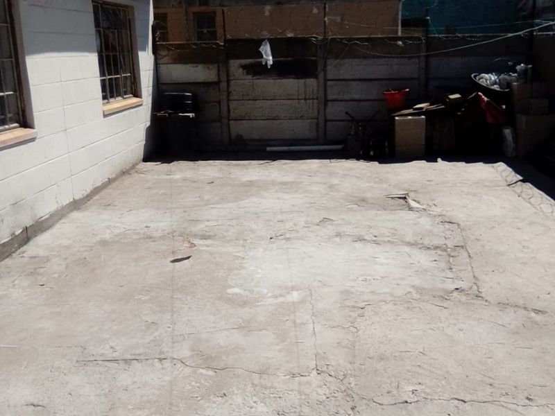 A rear exterior area featuring a concrete paved surface and a precast concrete boundary wall, showing signs of wear and surface cracking.