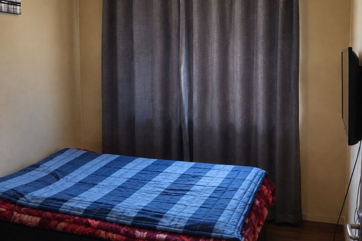 A compact bedroom featuring laminate flooring and a curtain rod, with visible wear on the ceiling panels.
