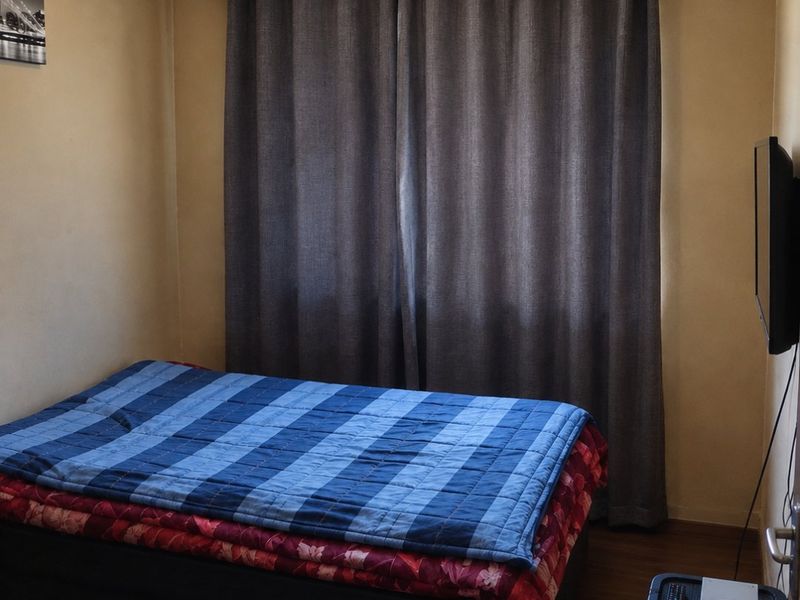 A compact bedroom featuring laminate flooring and a curtain rod, with visible wear on the ceiling panels.